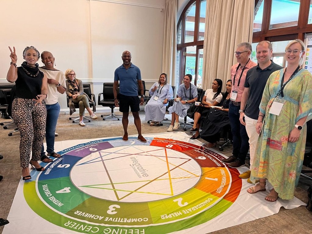 A leadership team gathered around a large Enneagram floor map during a team development session, with Robert Stephenson standing within the group
